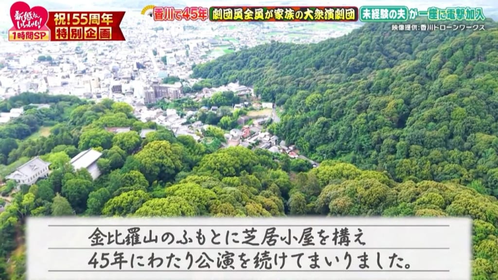 Aerial view of a forested hillside with a town at the base; handwritten caption in Japanese describes building a theater at the foot of Mount Kanpiray and continuing performances for 45 years.