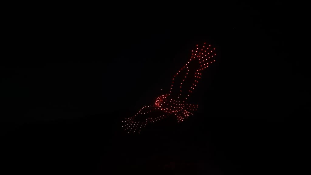 Red LED dot sculpture in the night sky forming a bird in flight against a dark background.