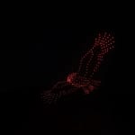 Red LED dot sculpture in the night sky forming a bird in flight against a dark background.