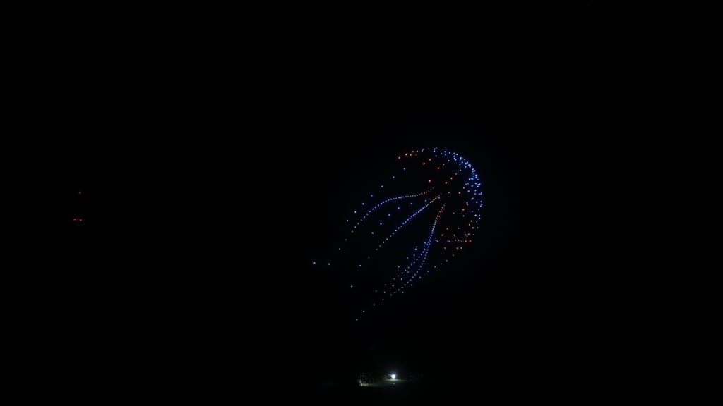 Dark night sky with a circular display of blue and red lights resembling a fireworks burst.