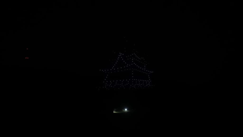 Dark night scene with blue LED lights arranged in a large tree shape above a small illuminated base.