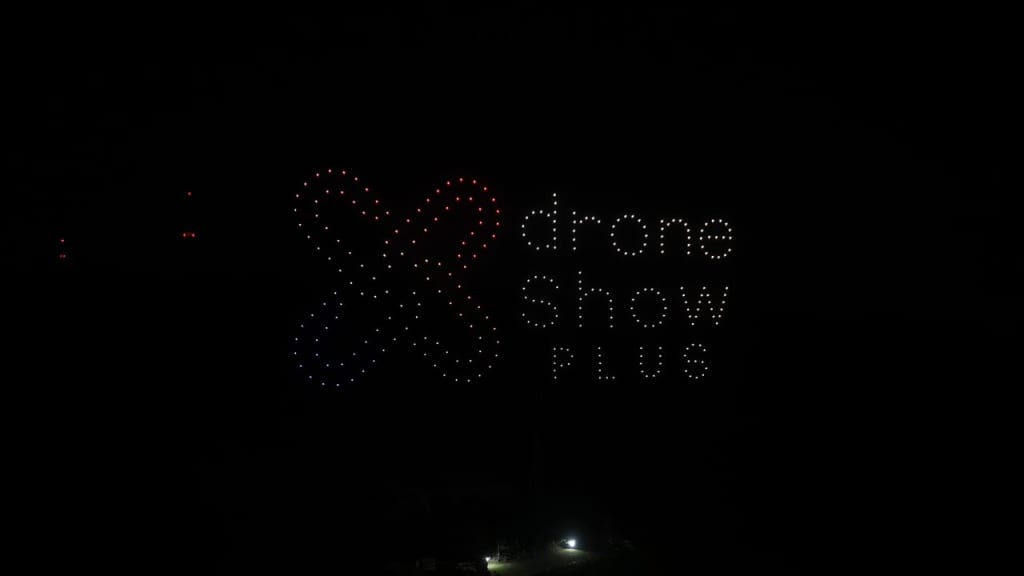 Drone light show signage formed by illuminated dots, reading 'drone show' with a heart shape on the left in red/blue lights.