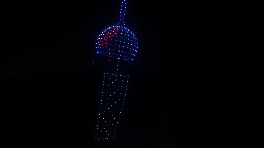 LED light sculpture at night: a tall column of blue dots with a glowing blue-topped sphere above, in red/green accents.