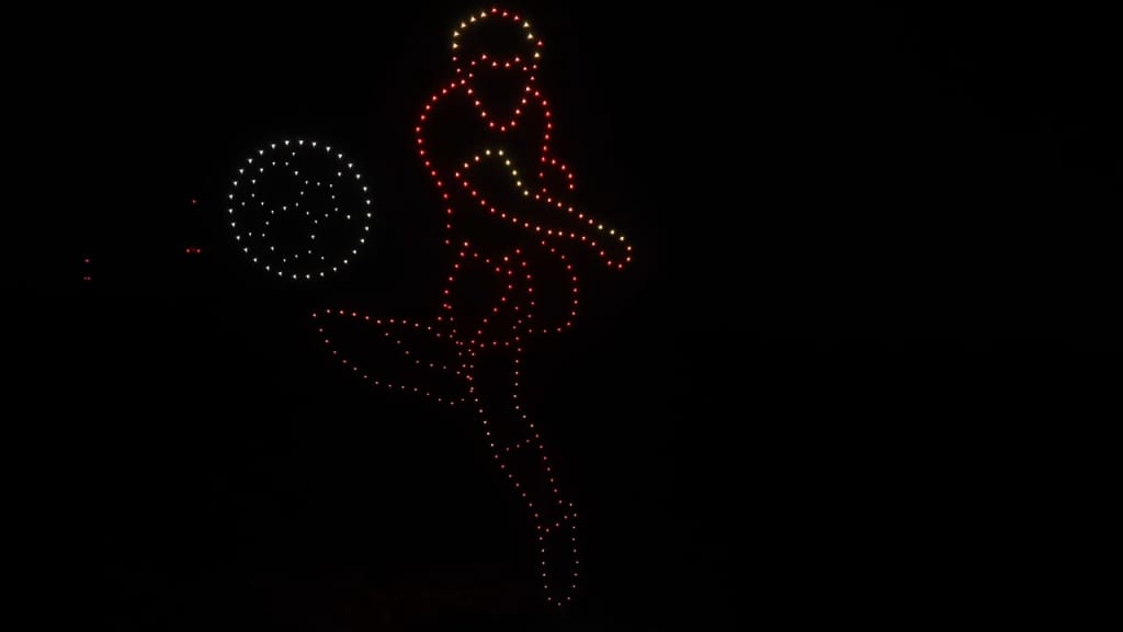 Red LED-dotted silhouette of a person dancing or leaping with a circular hoop and a glowing ball to the left, against a dark background.