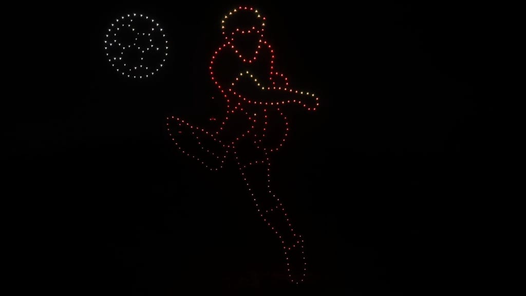 LED light sculpture of a person kicking a ball against a dark night sky, formed by red and white points of light on the left.